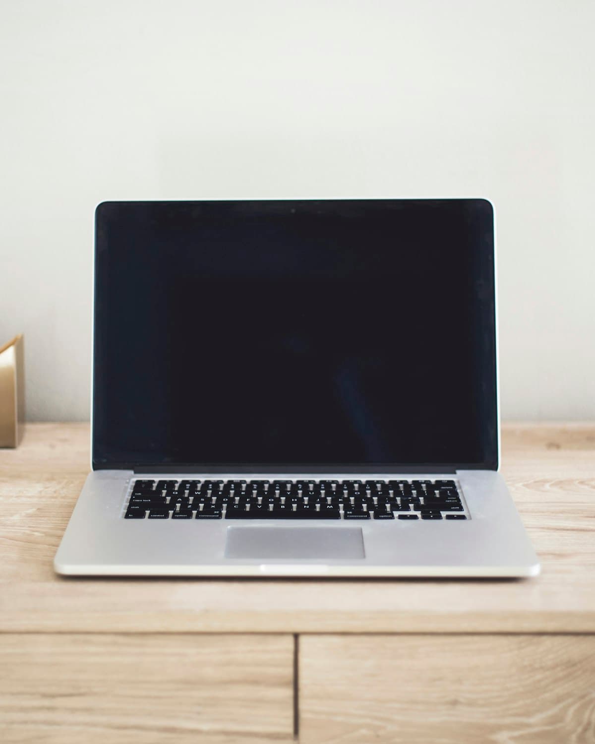 Silver laptop open on a light wood desk against a white wall